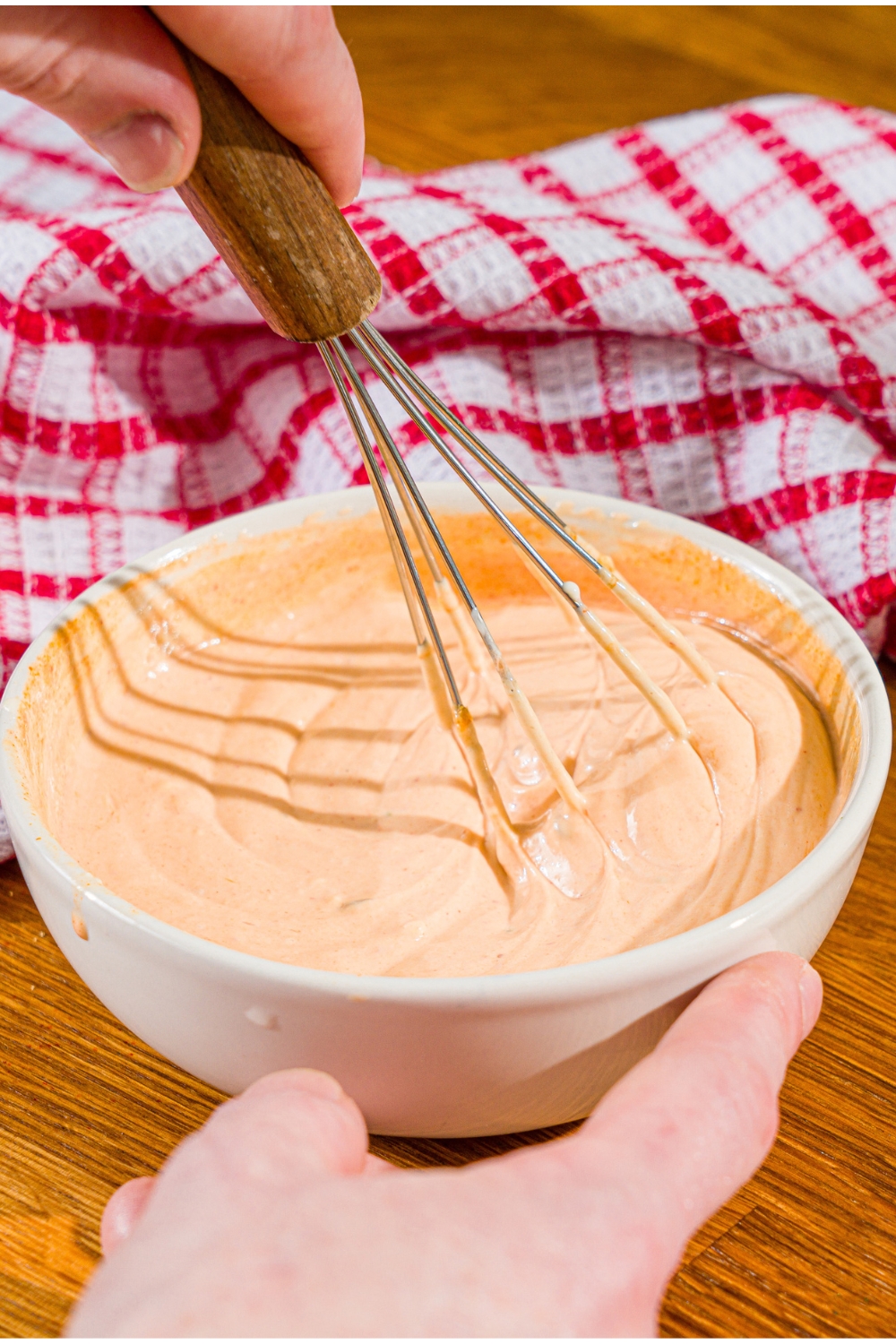 A whisk whisking comeback sauce that is in a white bowl with a hand holding in it.