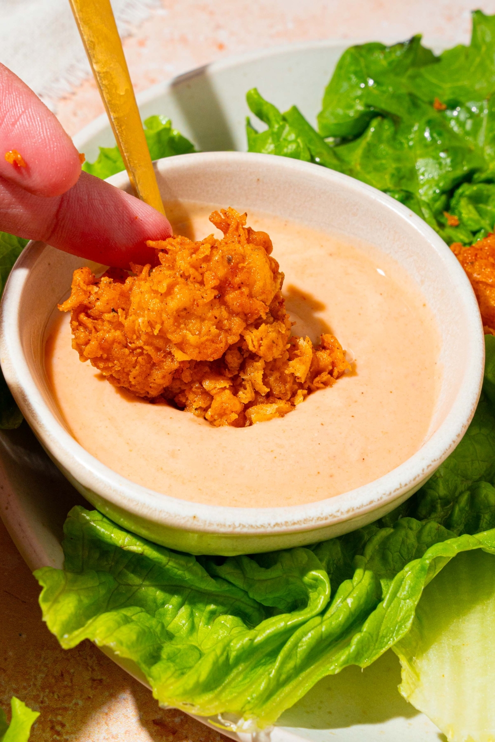A hand holding a chicken tender, dipping it into a white cup filled with Dave's hot chicken sauce.