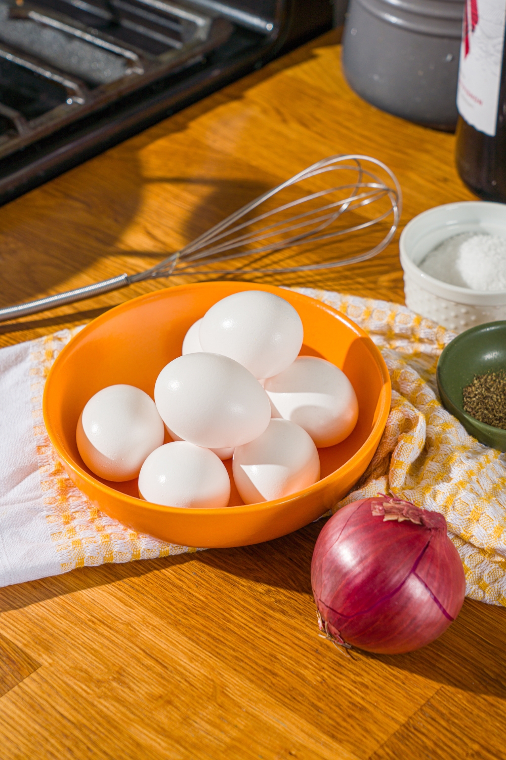 A bunch of eggs in an orange bowl and an onion.