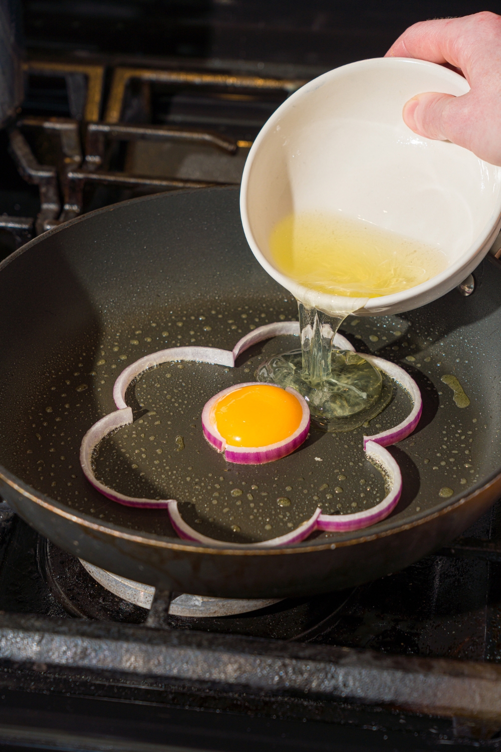 A hand holding a white bowl pouring egg whites inside