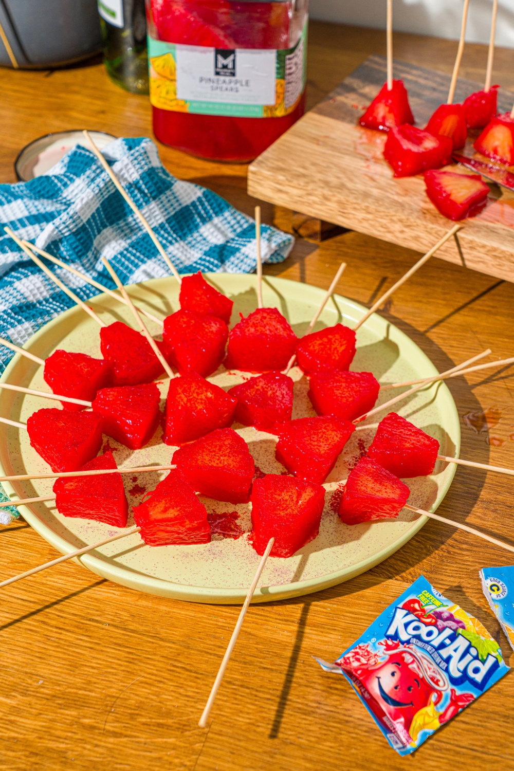 A bunch of sliced Kool-Aid pineapple spears with a toothpick in them on a green plate.