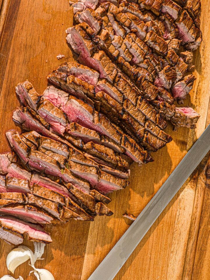 A london broil sliced into a bunch of thin slices on a wooden cutting board.