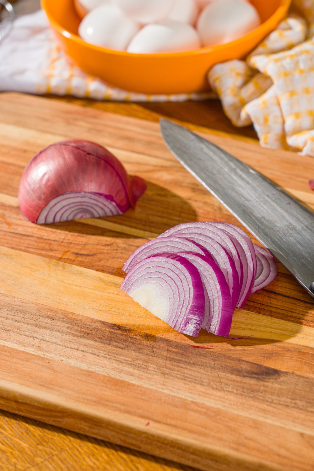 Half an onion and half an onion sliced on a wood cutting board.