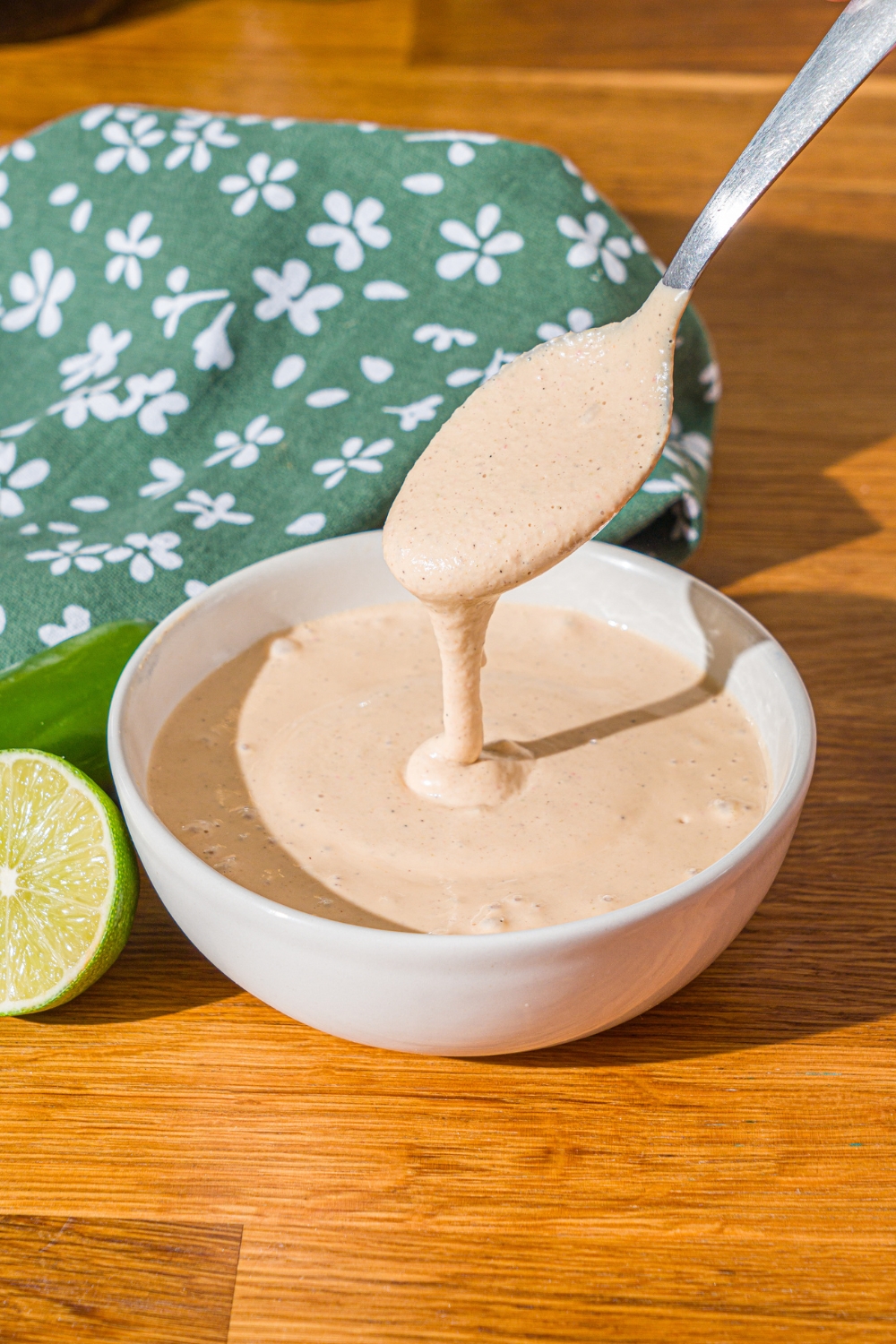 A spoon drizzling Baja sauce into a white bowl that is filled with the Baja sauce.