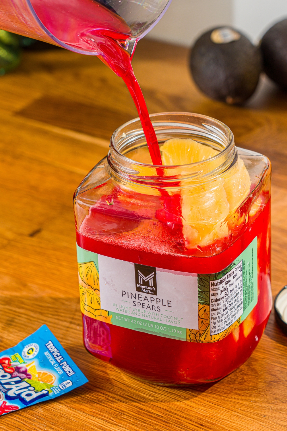 Red Kool-Aid being poured into a pineapple jar.