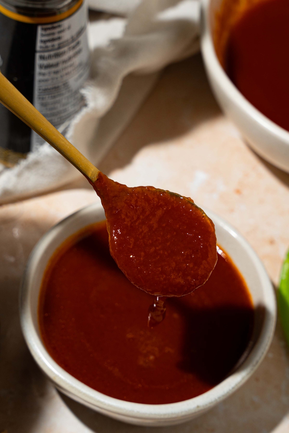 A small bowl of copycat Bachan Japanese BBQ sauce. A spoon is dipping into the bowl. The bowl is on a tan counter with a white cloth napkin and large bowl of sauce.