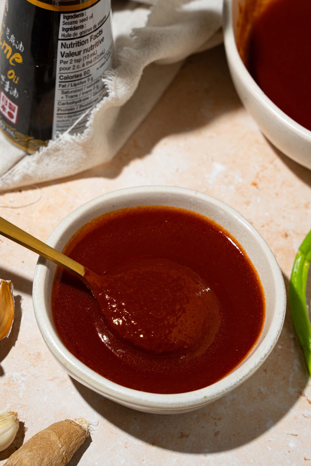 A bowl of copycat Bachan Japanese BBQ sauce with a spoon in the sauce. The bowl is on a tan counter with a white cloth napkin and large bowl of sauce.