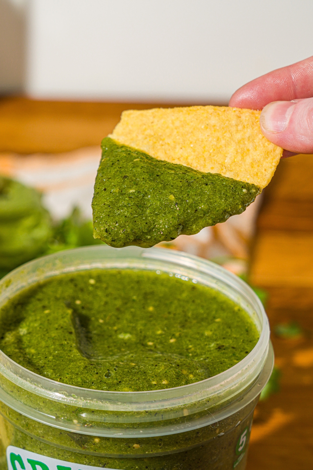 A chip dipped in Grillo's pickle salsa stored in a Grillo's pickles container. The container is on a wooden counter.