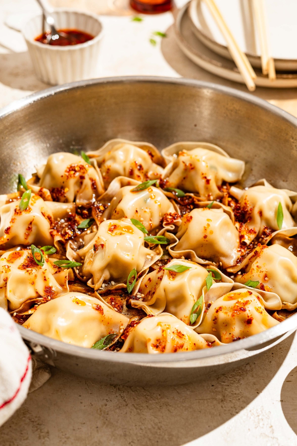 A skillet with blanket dumplings topped with chili crisp, sesame seeds, and sliced green onion. The skillet is on a tan counter.