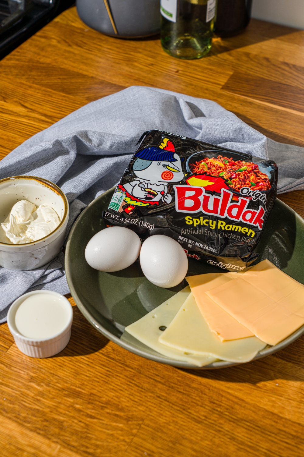 A plate with Buldak ramen packet, eggs, American cheese, Jarlesberg cheese, cream cheese, and heavy cream.