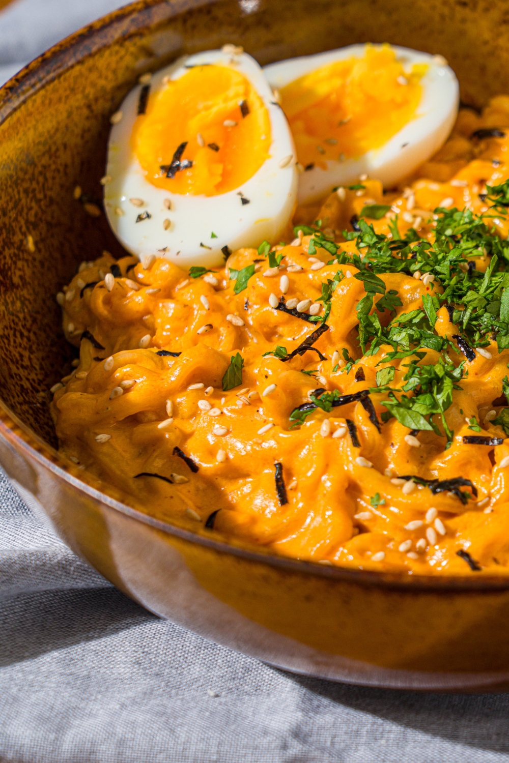 A bowl of Buldak ramen with soft boiled egg and garnished with fresh parsley and sesame seeds. The bowl is on a wooden counter with a blue cloth napkin.