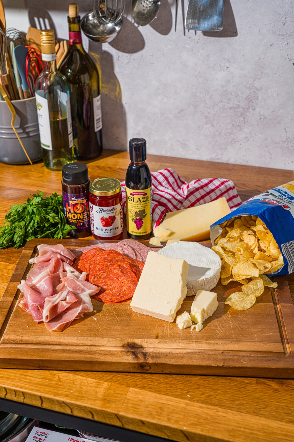 A wooden cutting board with ingredients to make charcuterie nachos including kettle chips, salami, prosciutto, pepperoni, brie cheese, cheddar cheese, fresh basil, and more.
