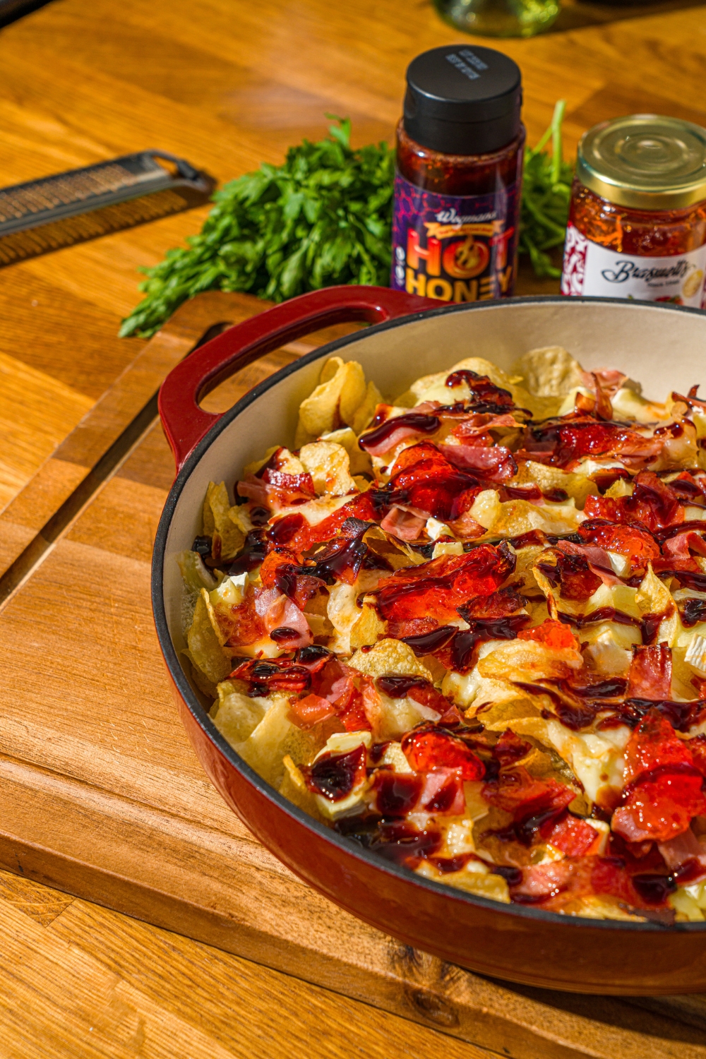 A baking dish with baked charcuterie nachos topped with balsamic glaze. The dish is on a wooden counter with jars of toppings.