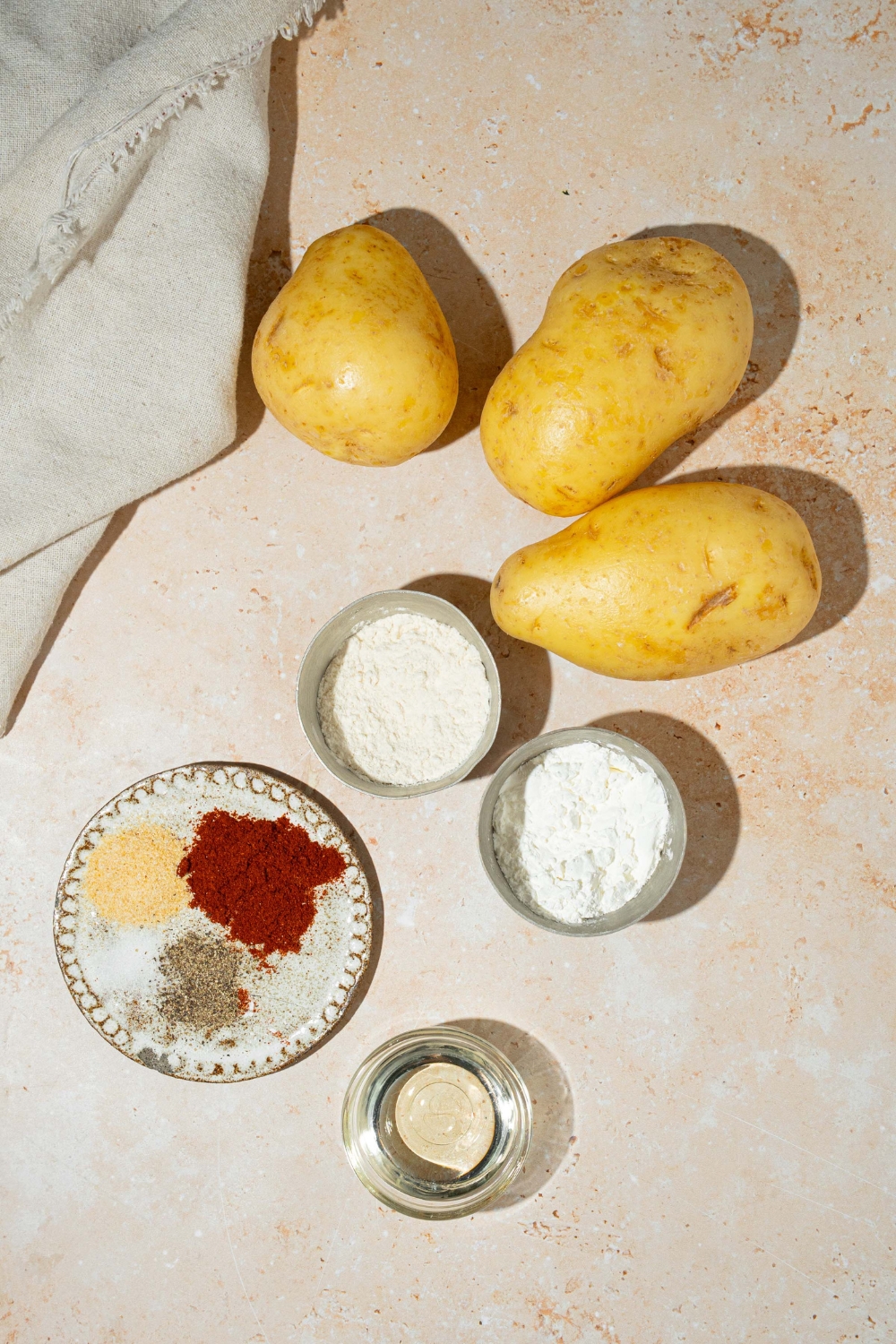 A tan counter with ingredients to make cheesy fiesta potatoes including potatoes, cornstarch, flour, oil, and seasonings.