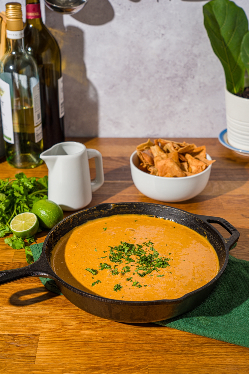 A Chili's skillet queso topped with chopped cilantro. The skillet is on a wooden counter with lime, fresh cilantro, and bowl of chips.
