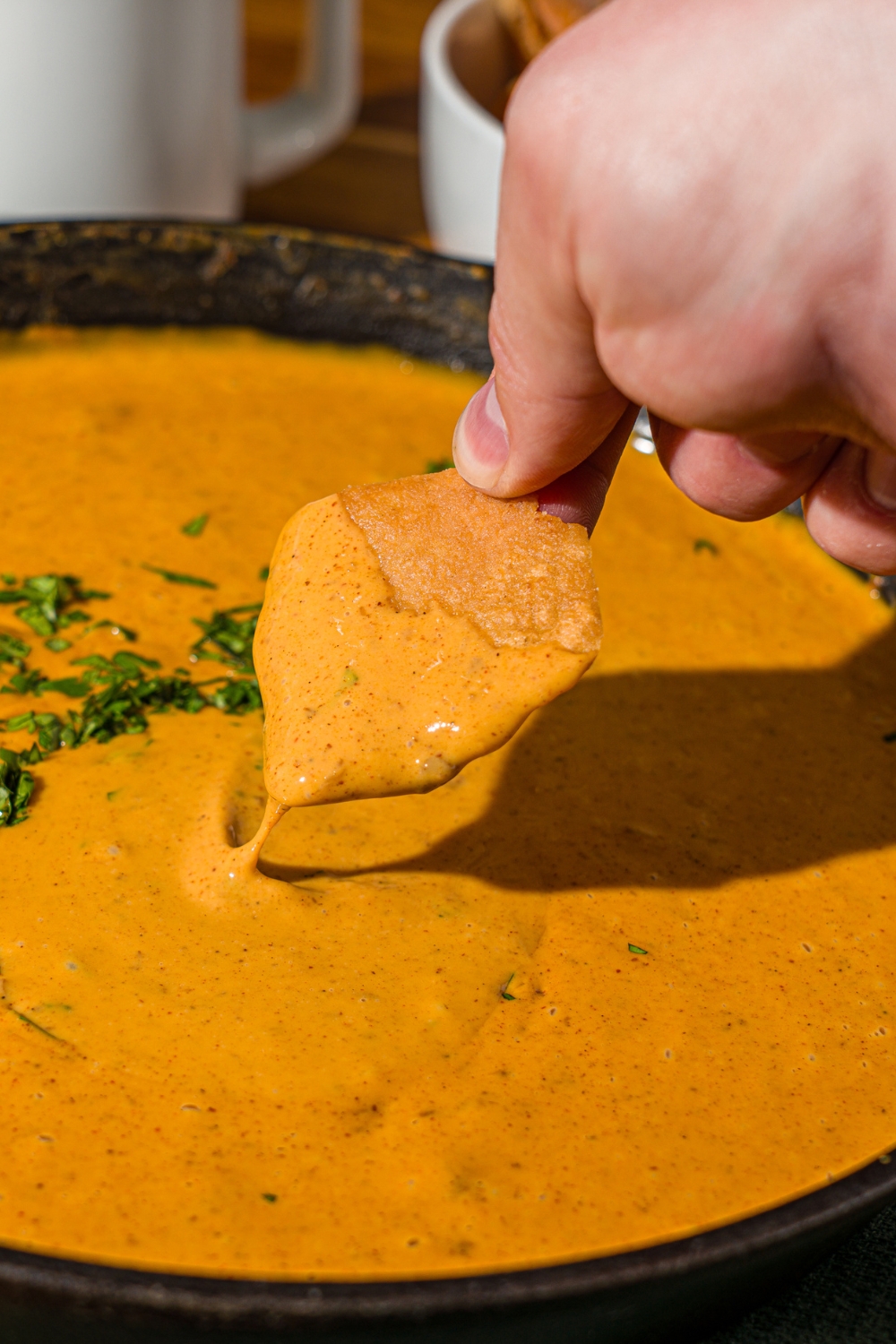 A hand dipping a chip into a skillet with Chili's skillet queso. The queso is garnished with fresh cilantro.