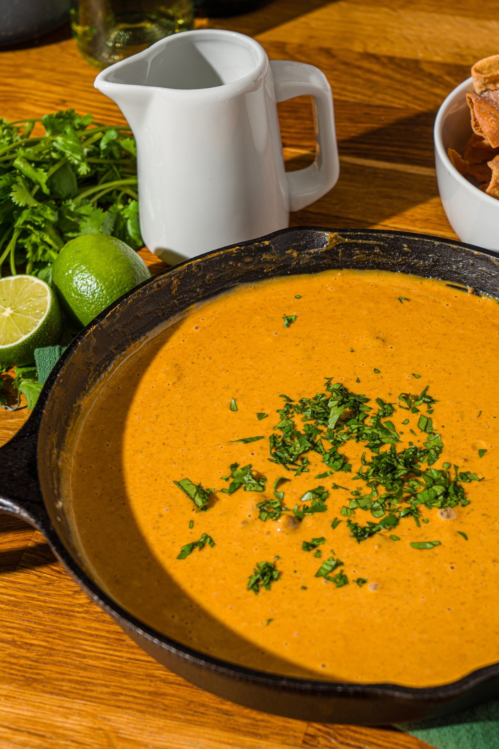 A skillet with Chili's skillet queso garnished with fresh cilantro. The skillet is on a wooden counter with fresh cilantro, lime, and a bowl of chips.