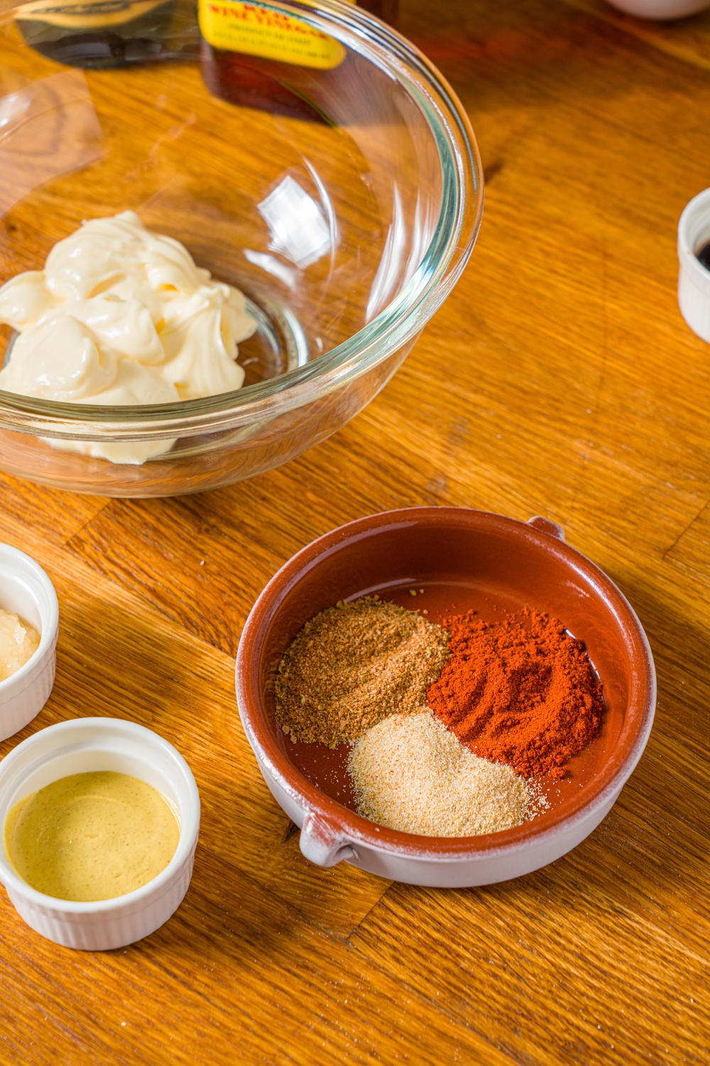 A wooden counter with bowls containing ingredients to make crab cake sauce including mayonnaise, dijon mustard, and seasonings.