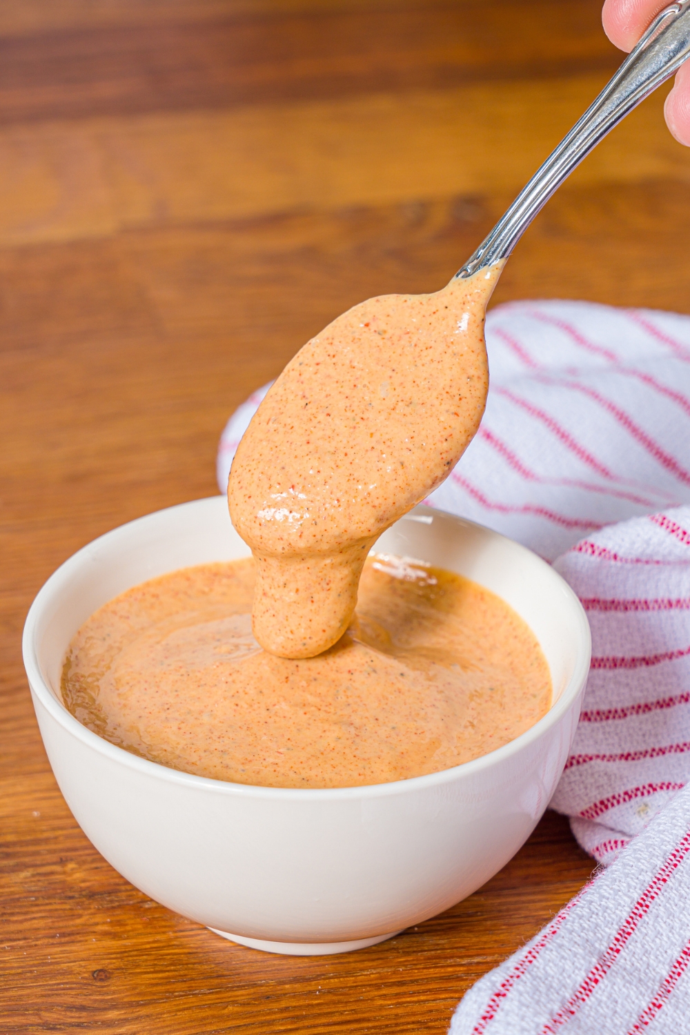 A bowl of crab cake sauce with a spoon dipping into the bowl. The bowl is on a wooden counter with a red striped napkin.