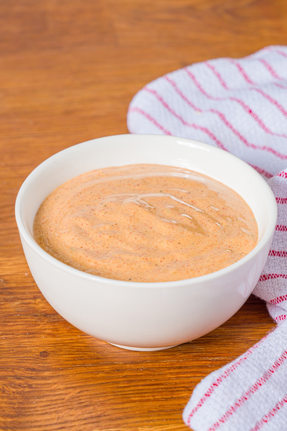 A small bowl of crab cake sauce on a wooden counter with a red striped napkin.