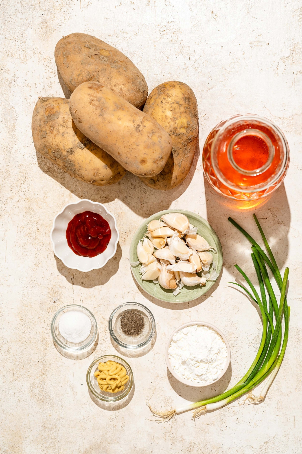 A tan counter with ingredients to make Japanese long fries including potatoes, cornstarch, garlic, water, ketchup, green onion, oil, and seasonings.