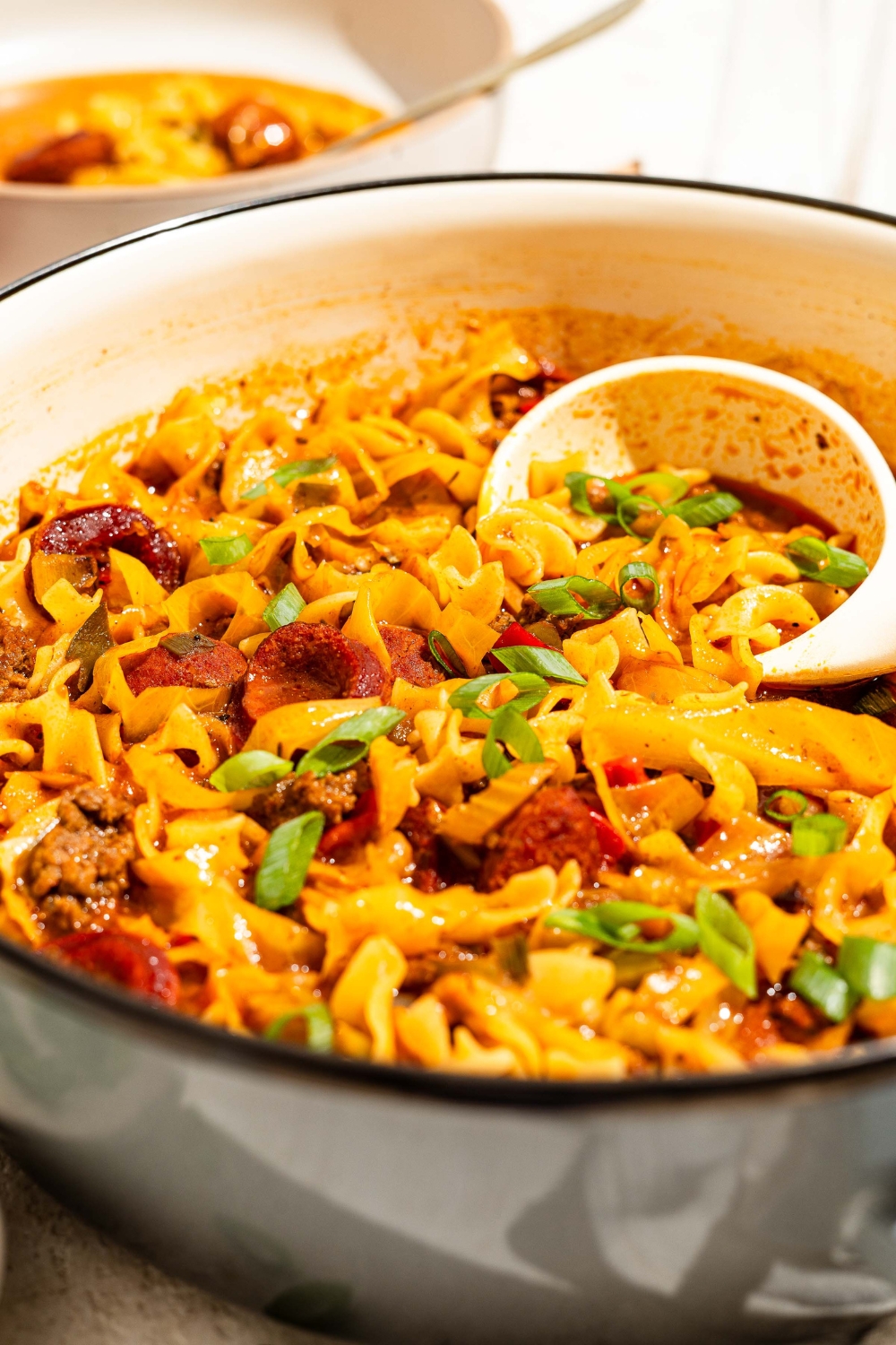 A dutch oven of dirty cabbage and noodles with a ladle taking noodles from the bowl. The dutch oven is on a tan counter.