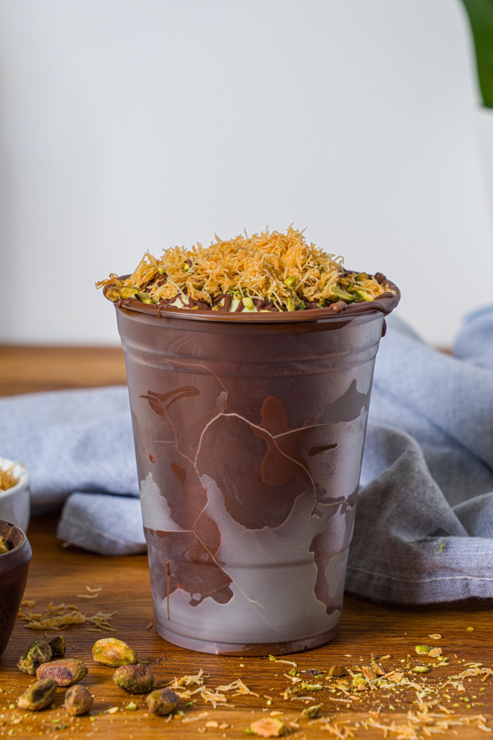 A Dubai chocolate shake shake shack copycat that is in a chocolate lined clear cup. On top of the shake is some drizzle, chocolate, pistachios, and katafi.