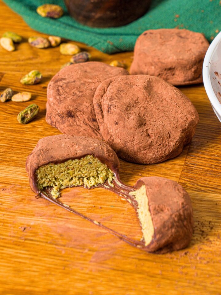 A Dubai cookie broke in half with three chewy Dubai chocolate cookies behind them, all on a wood counter.