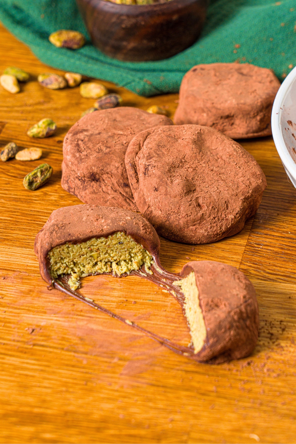 A Dubai cookie broke in half with three chewy Dubai chocolate cookies behind them, all on a wood counter.