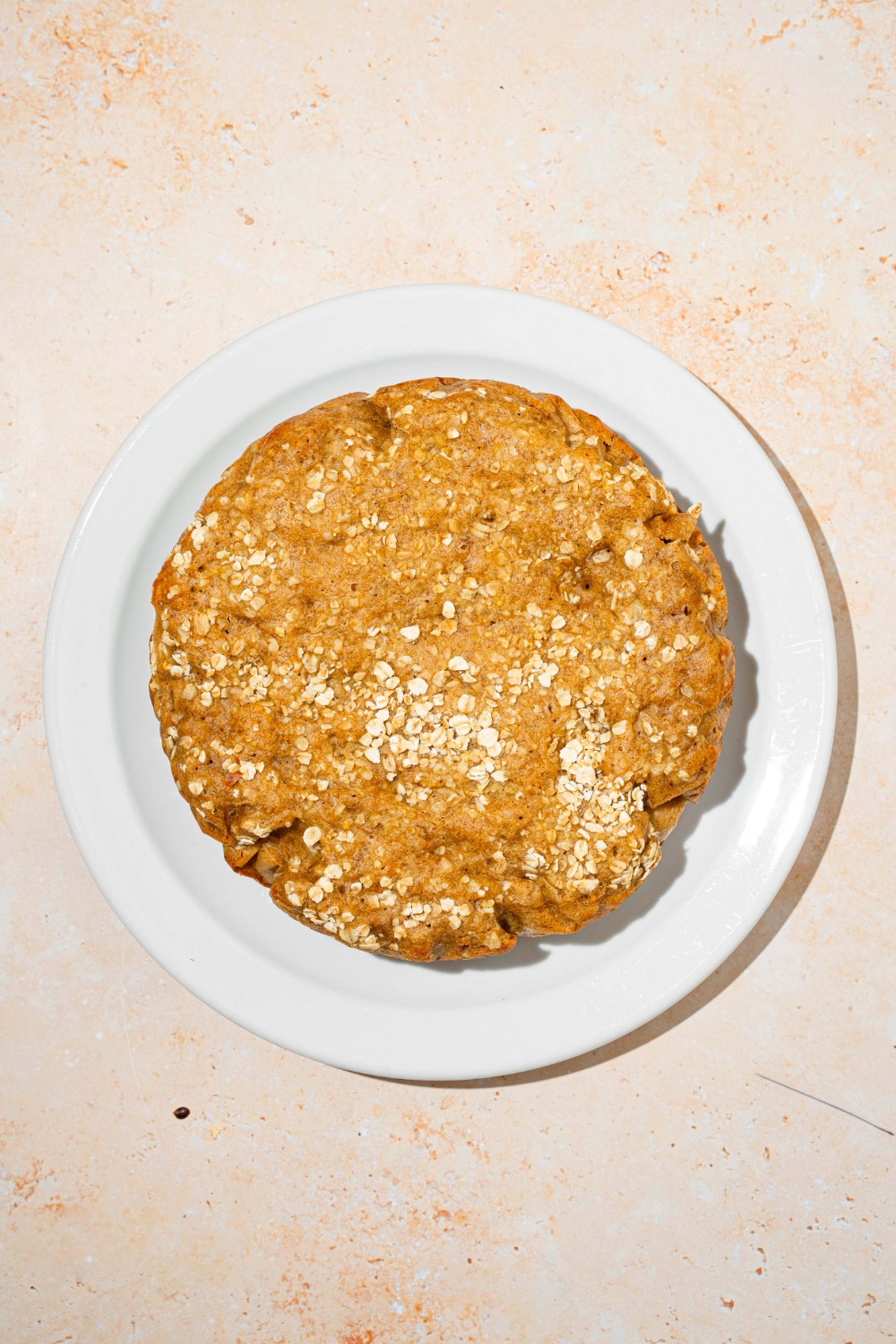 A circular rice cooker banana bread loaf on a white plate on top of a cream counter top.