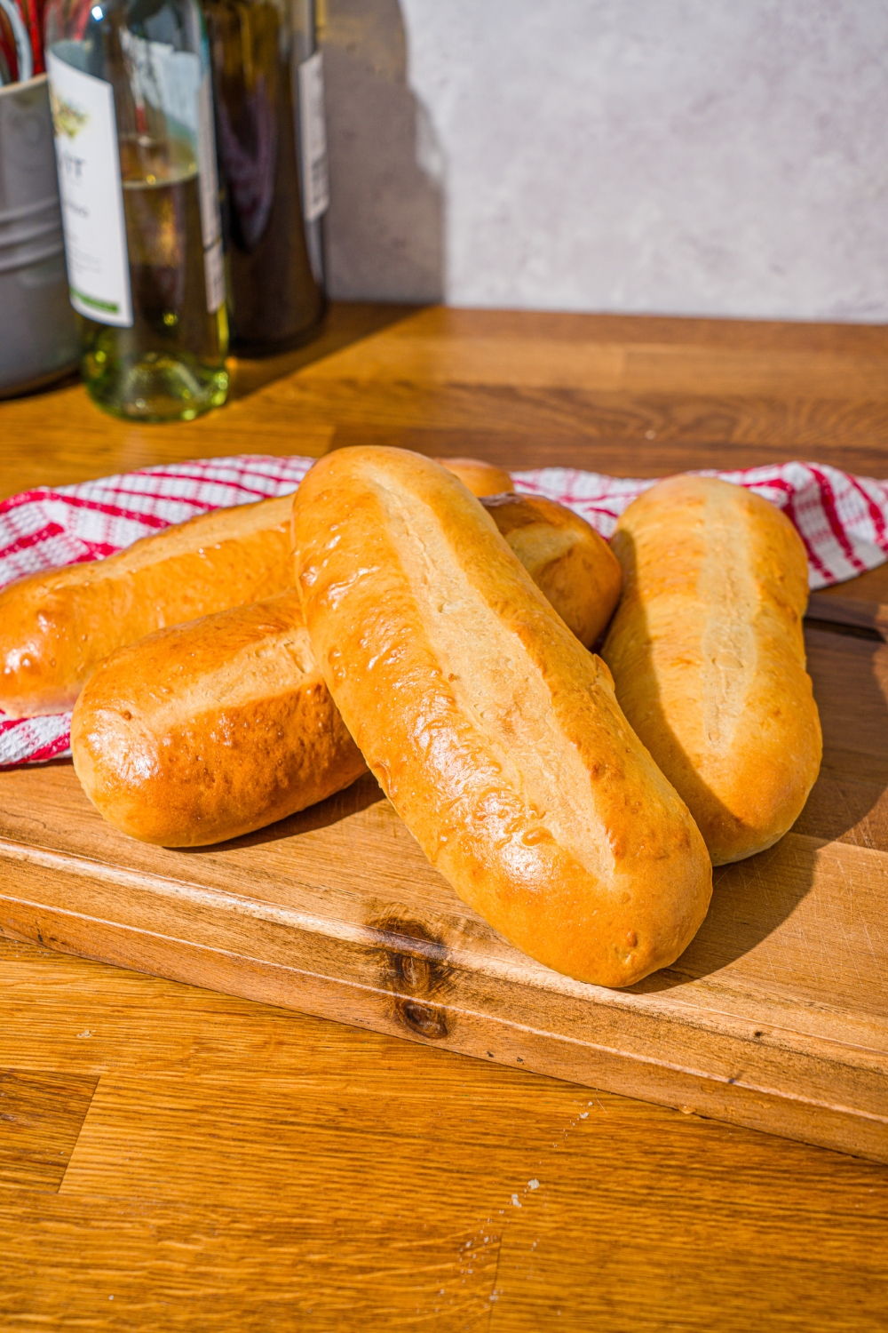 A wooden board with homemade hoagie rolls. The board is on a wooden counter with a red striped napkin.