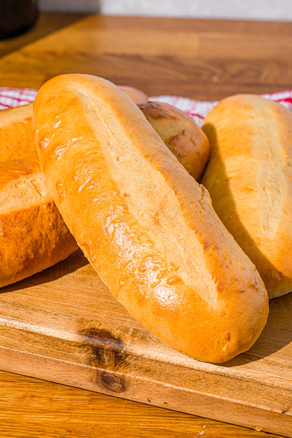 A wooden board with homemade hoagie rolls. The board is on a wooden counter with a red striped napkin.
