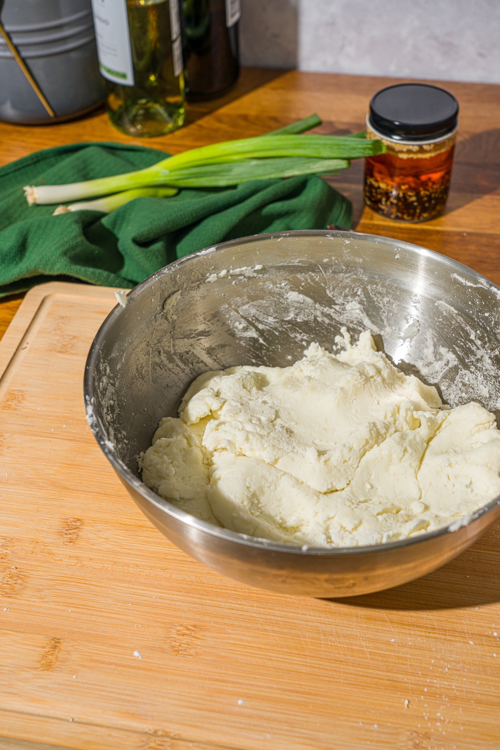A large mixing bowl with spicy potato noodle dough. The bowl is on a wooden cutting board. The board is on a wooden counter with a green cloth napkin.
