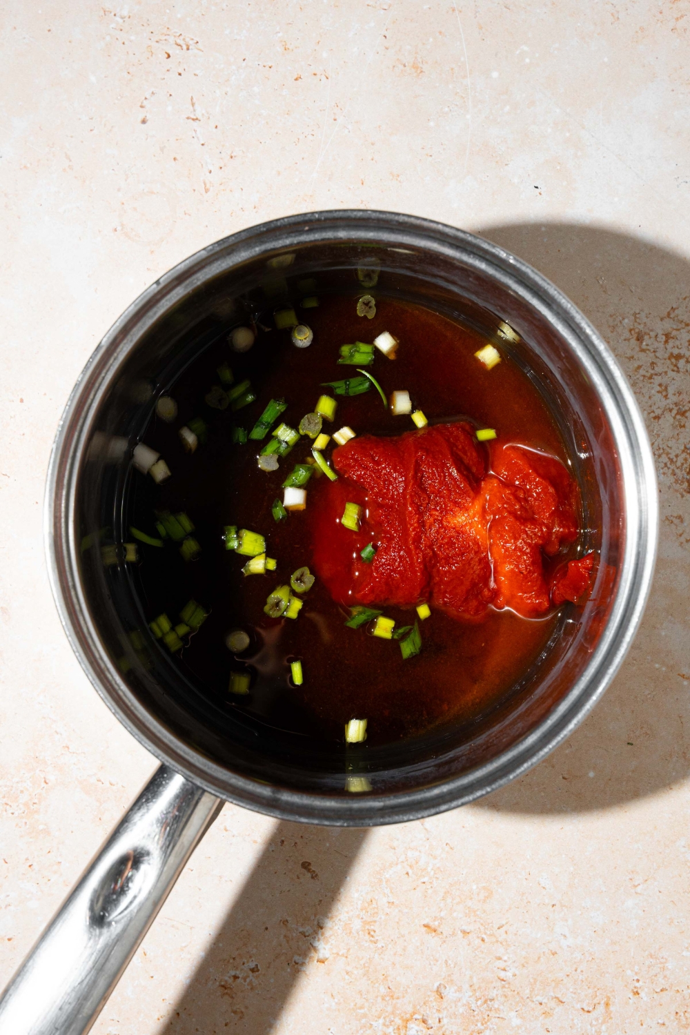 A pot with a soy sauce mixture with brown sugar, tomato paste, mirin, and chopped green onion. The pot is on a tan counter.
