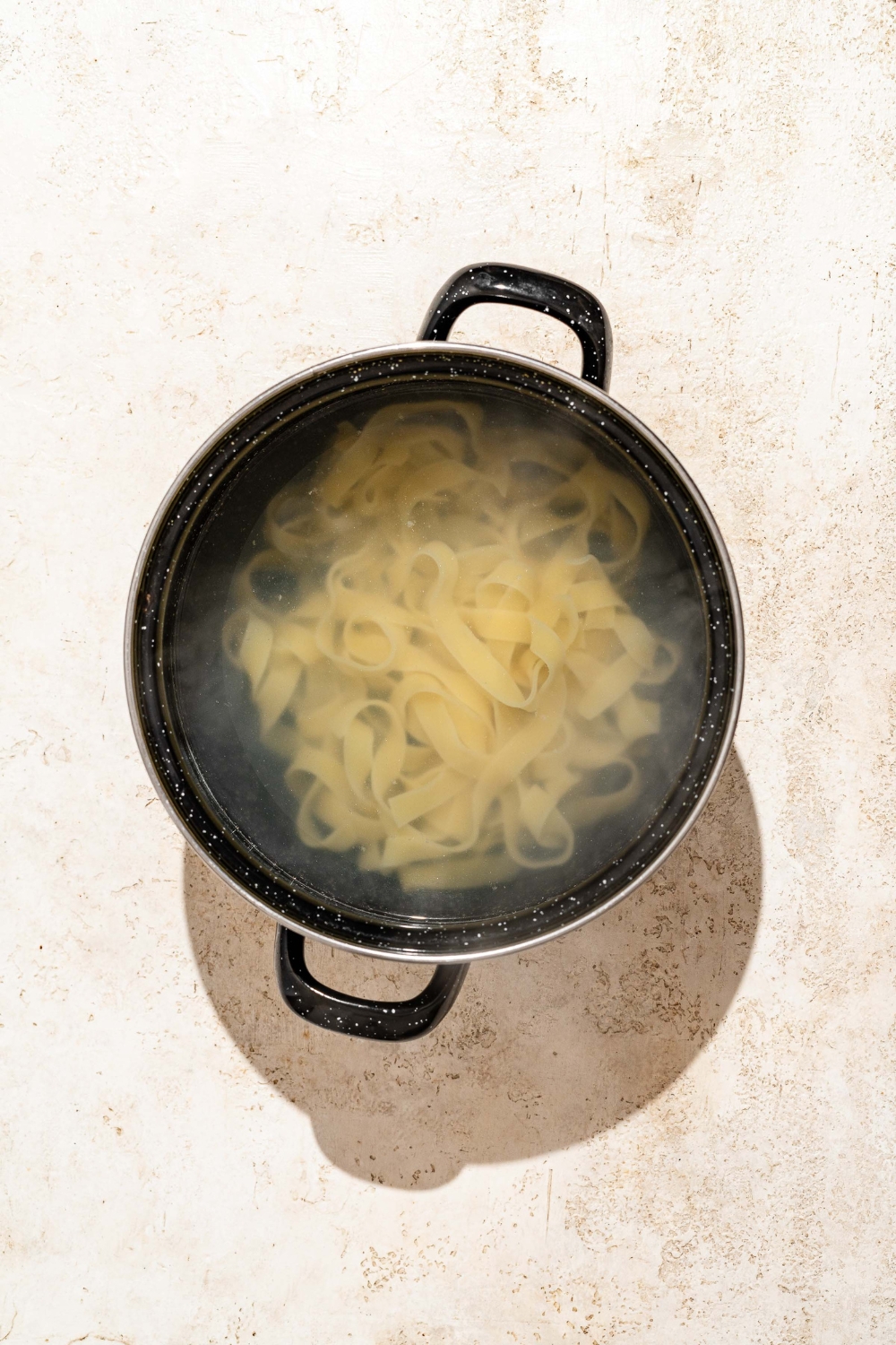 A large pot with fettuccine pasta in water. The pot is on a tan counter.