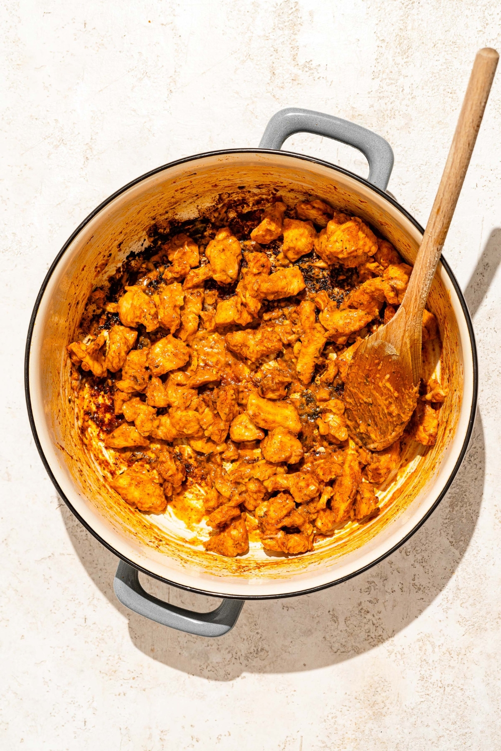 A dutch oven with creamy Buffalo chicken. There is a wooden spoon in the pot.