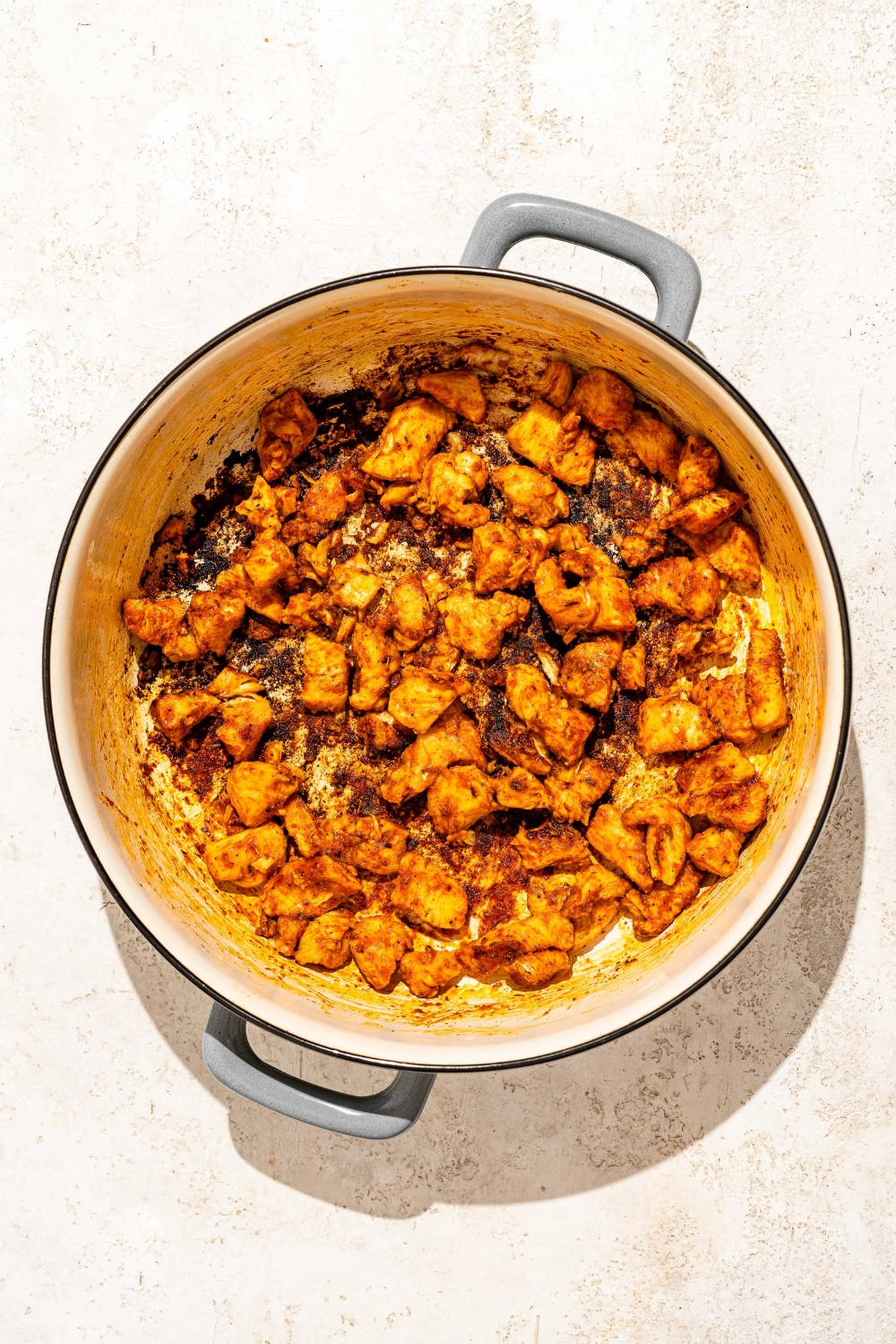A dutch oven with seared Buffalo chicken. The dutch oven is on a tan counter.