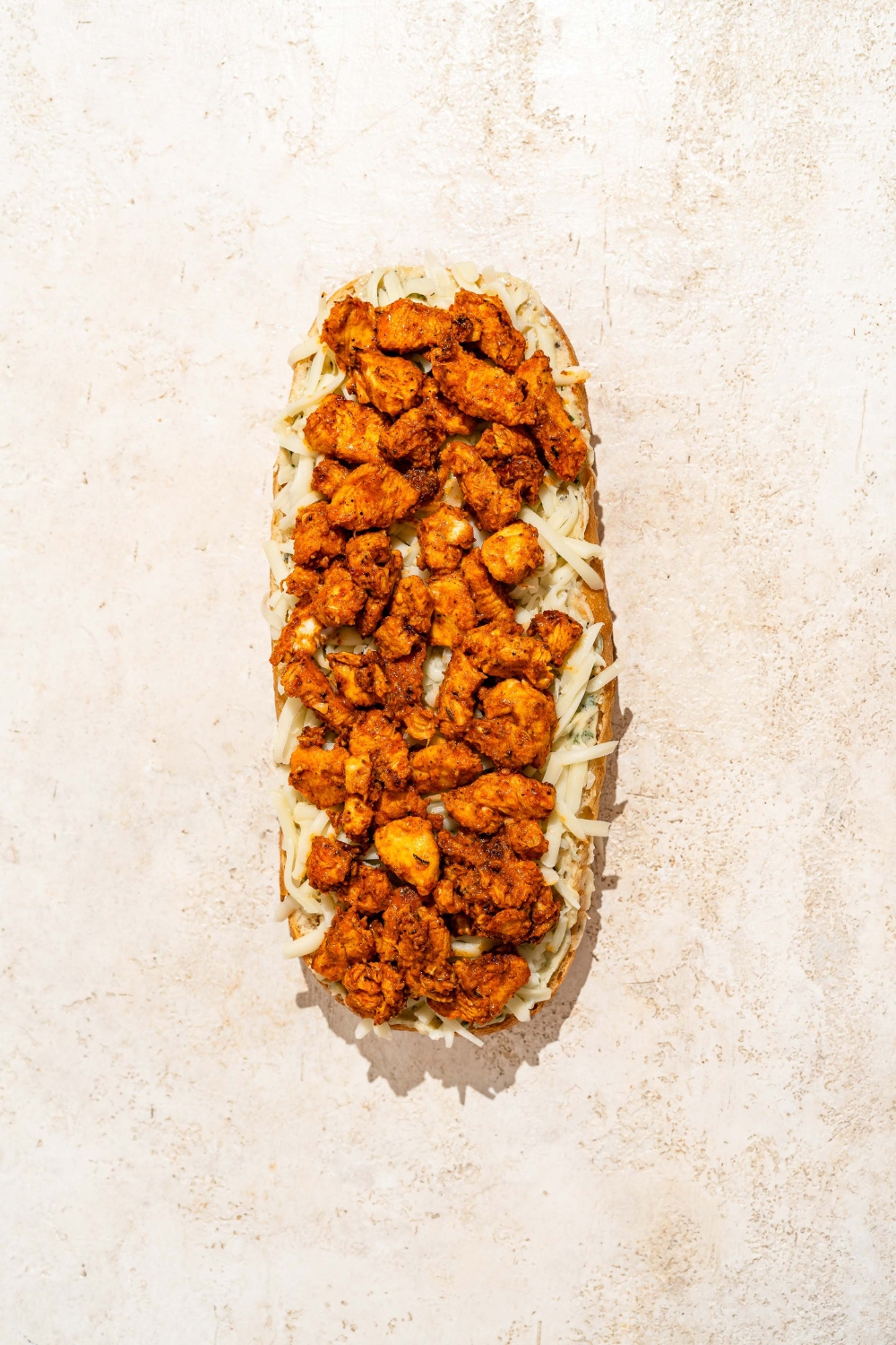 A slice of Italian bread loaf topped with garlic butter and seasoned Buffalo chicken.