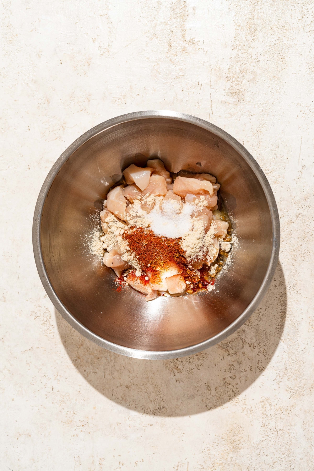 A large bowl with uncooked chicken breast topped with garlic powder, onion powder, paprika, salt and pepper, and more.