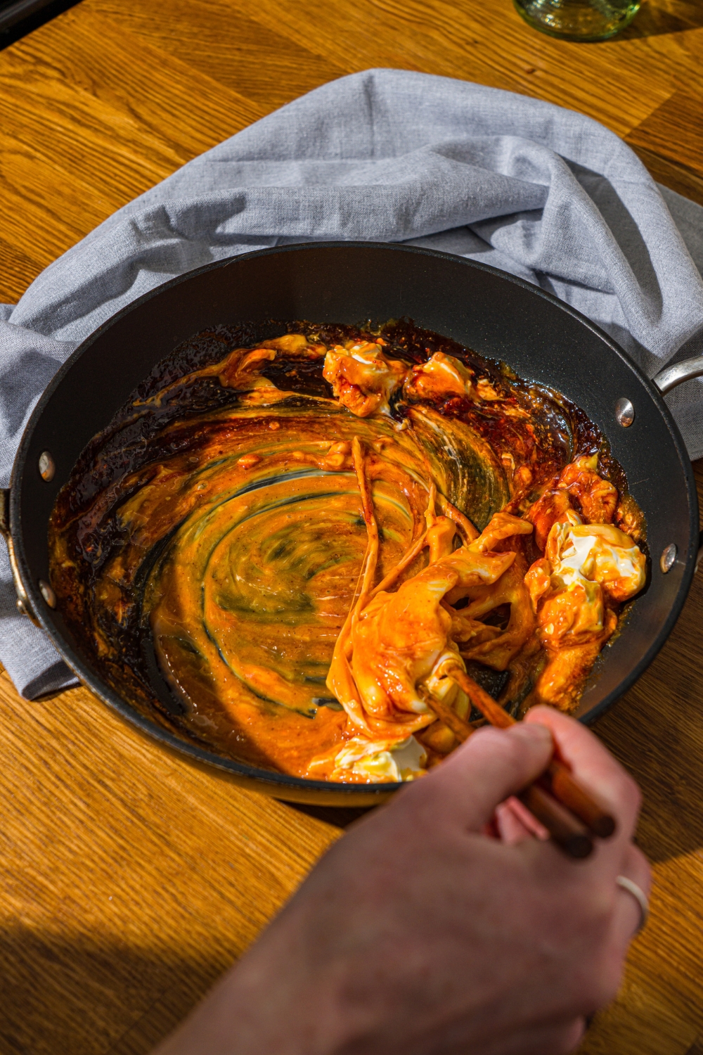A skillet with a pair of chopsticks stirring melted cheese, Buldak sauce, and egg yolks. The skillet is on a wooden counter with a blue cloth napkin.