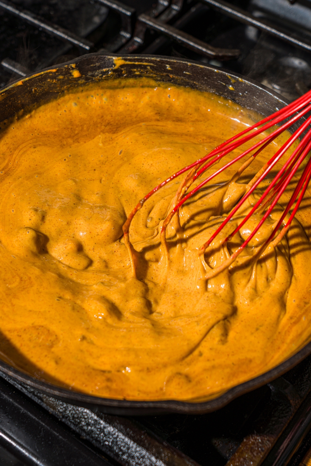 A skillet with a whisk mixing ingredients to make Chili's skillet queso including Hormel chili, Velveeta, milk, and seasonings. The skillet is cooking on the stove.