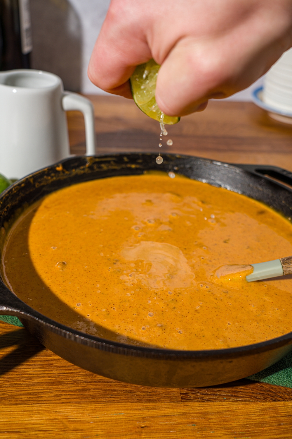 A skillet with Chili's skillet queso with a spatula in the queso. A hand is squeezing lime into the queso. The skillet is on a wooden counter.