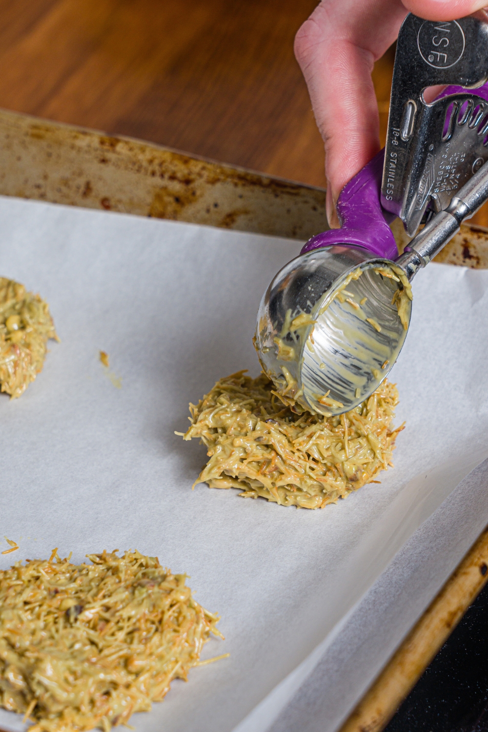 A scooper placing pistachio filling pieces on a baking sheet lined with parchment paper.