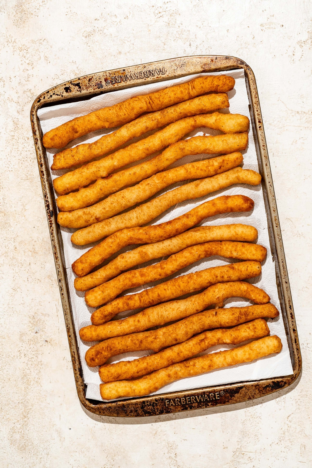 A baking sheet lined with parchment paper with fried Japanese long fries. The sheet is on a tan counter.