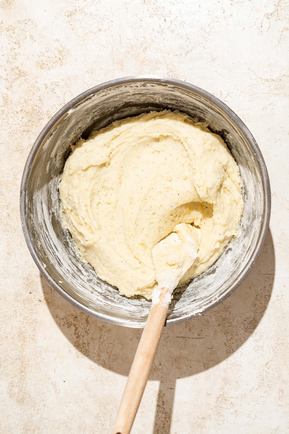 A large bowl with a wooden spoon mixing Japanese long fries dough. The bowl is on a tan counter.