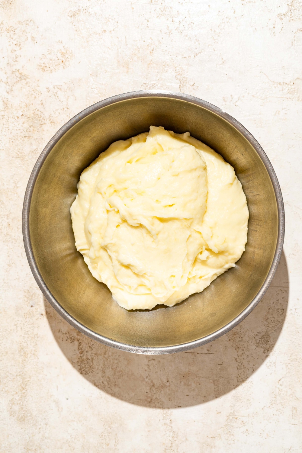 A large bowl with mashed potatoes. The bowl is on a tan counter.