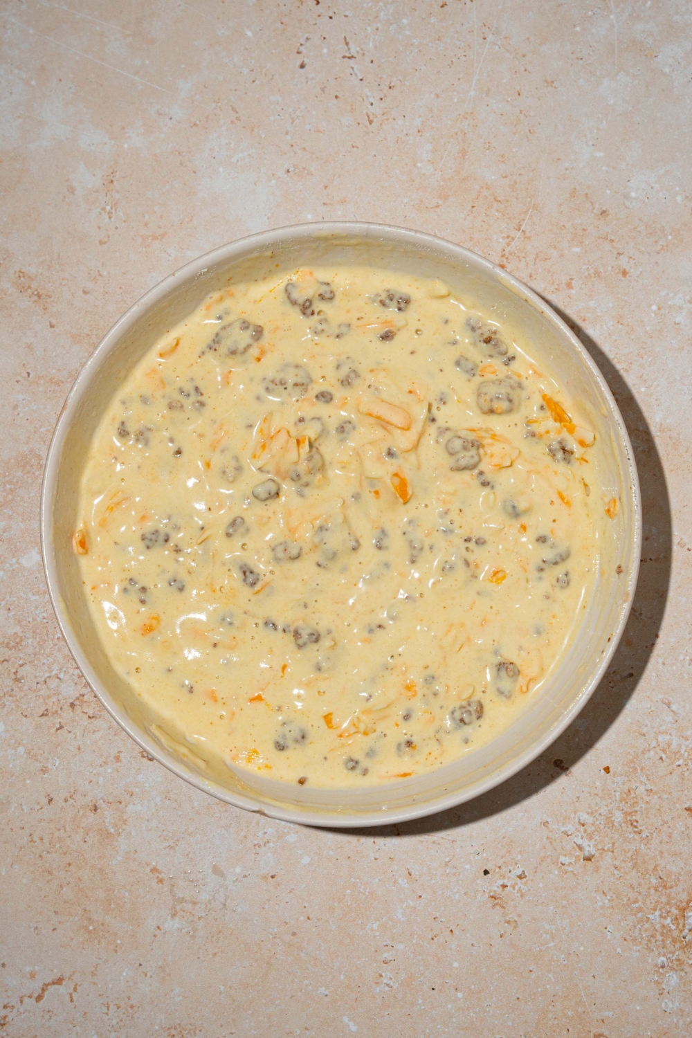 A large bowl with McGriddle muffin batter tossed with sausage, cheese, and syrup. The bowl is on a tan counter.