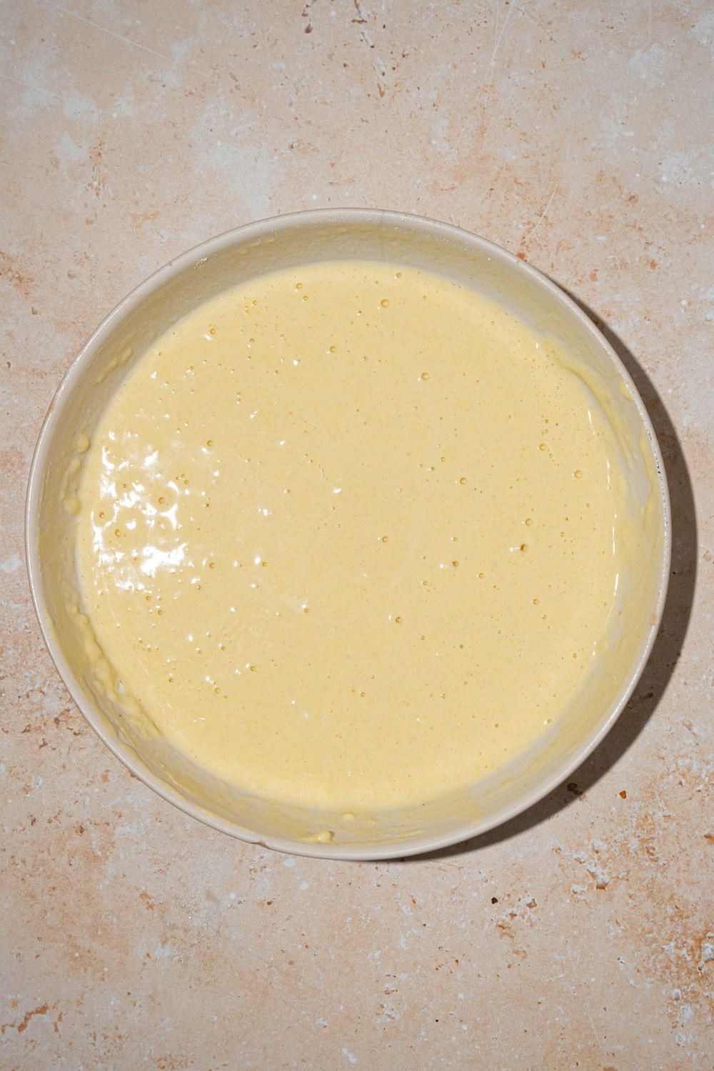 A large white bowl with pancake batter. The bowl is on a tan counter.