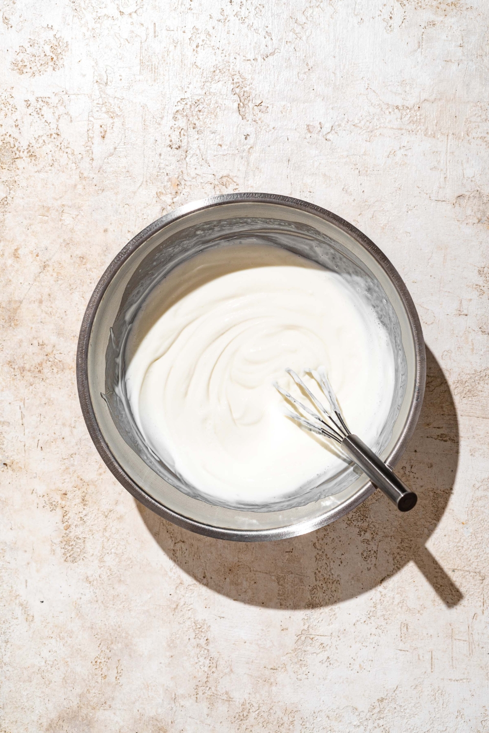A large bowl with a whisk mixing mayo and buttermilk. The bowl is on a tan counter.