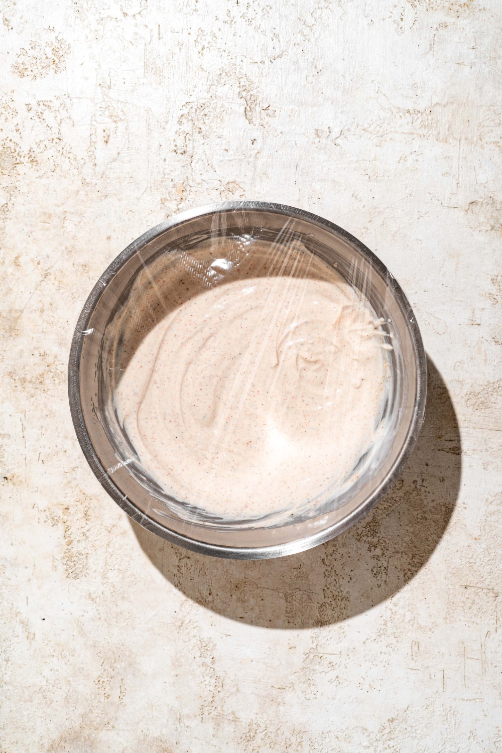A large bowl with Outback ranch dressing covered in plastic wrap. The bowl is on a tan counter.